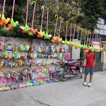Children browse through a colourful display of plastic toys including toy cars, push toys and various playthings at a roadside toy stall