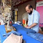 A skilled tailor marks and measures jeans for alterations at his roadside workshop