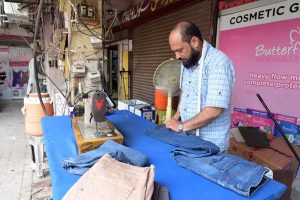 A skilled tailor marks and measures jeans for alterations at his roadside workshop