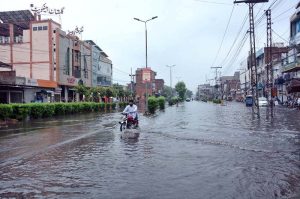 Motorcycles and tricycle rickshaws passing through rain water accumulated on the road after heavy rain in the city.