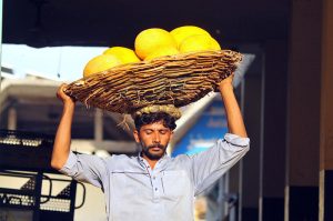 A daily-wage labourer carries a basket loaded with fresh melons on his head for delivery at a local fruit market in the city.