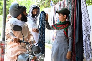 A young vendor displays and sells cotton handkerchiefs by the roadside during the severe summer heat