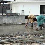Construction workers lay and level fresh concrete on the rooftop of a building under construction. Wearing rubber boots, the labourers carefully spread and smooth the concrete over steel reinforcement bars as construction activity continues across the twin cities despite the ongoing monsoon season