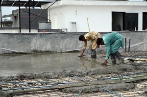 Construction workers lay and level fresh concrete on the rooftop of a building under construction. Wearing rubber boots, the labourers carefully spread and smooth the concrete over steel reinforcement bars as construction activity continues across the twin cities despite the ongoing monsoon season