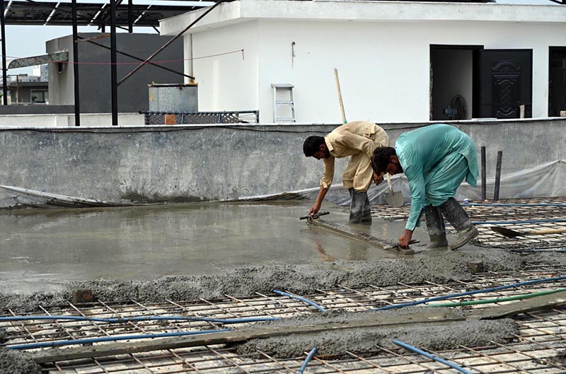 Construction workers lay and level fresh concrete on the rooftop of a building under construction. Wearing rubber boots, the labourers carefully spread and smooth the concrete over steel reinforcement bars as construction activity continues across the twin cities despite the ongoing monsoon season