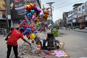 Children browse through a colourful display of plastic toys including toy cars, push toys and various playthings at a roadside toy stall