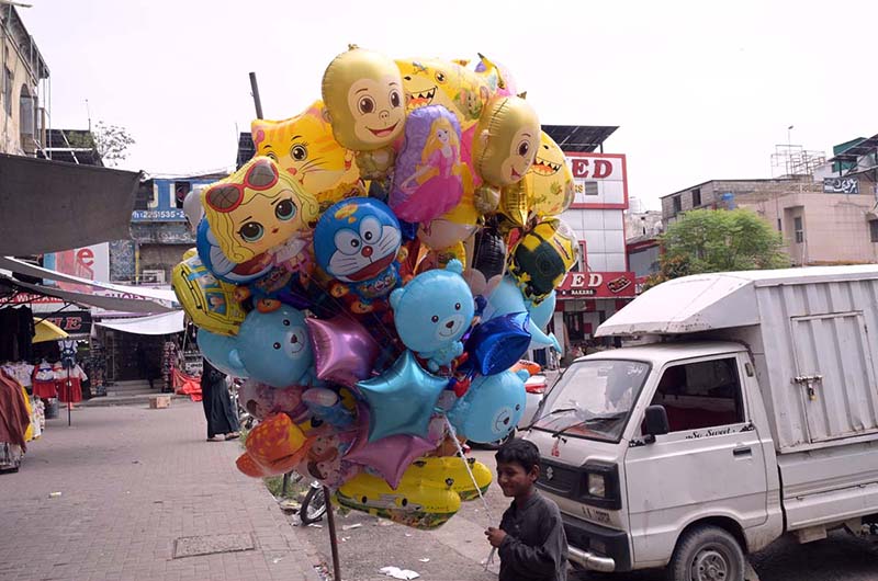 A young boy sells colourful foil balloons featuring popular cartoon characters including Doraemon, monkeys, sharks, bears and stars