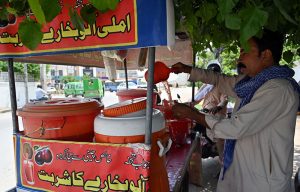 A vendor sells tamarind and plum juice by the roadside as people drink it to beat the intense summer heat