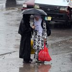 Girls share an umbrella while waiting for a bus on a waterlogged as monsoon rains lash in the Federal Capital