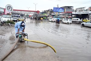 Girls share an umbrella while waiting for a bus on a waterlogged as monsoon rains lash in the Federal Capital