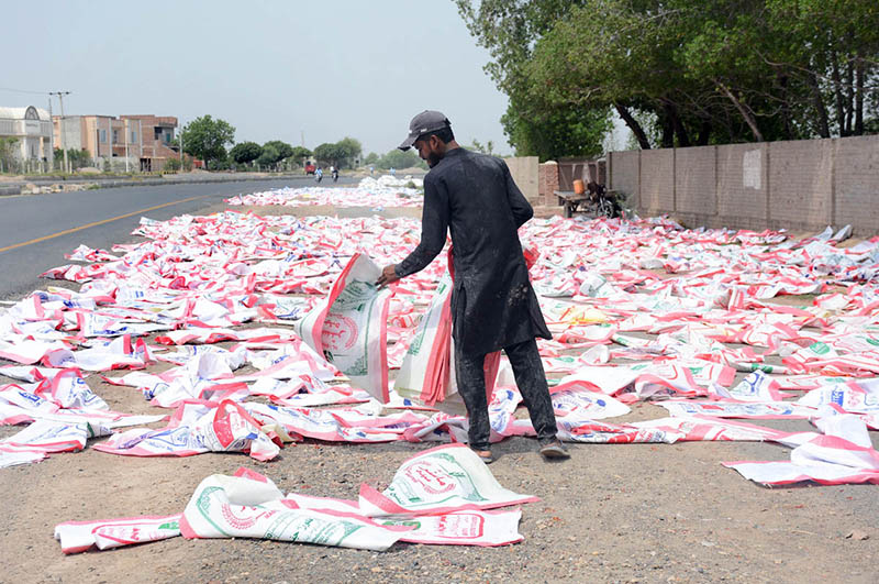 A worker spreads and arranges empty polypropylene sacks for drying under the sun along a roadside before they are reused for agricultural and commercial purposes in the city