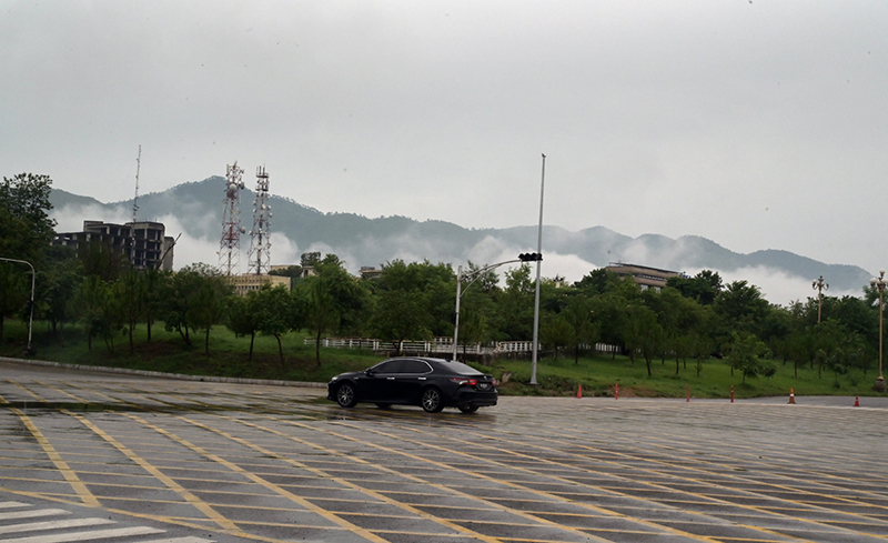 Low-lying clouds and mist blanket the Margalla Hills as a vehicle navigates through a rain-soaked road in Federal Capital following heavy monsoon rainfall