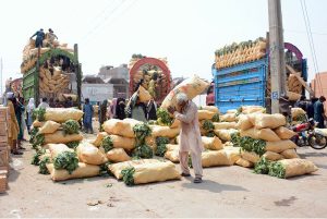 Labourers unload sacks of fresh leafy vegetables from trucks at the wholesale vegetable market for distribution to local markets in the city