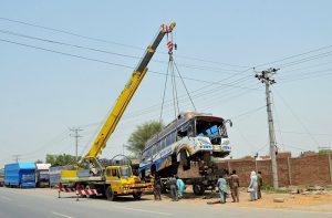 A crane lifts a damaged passenger bus during recovery operations after its axle broke down on the roadside, while mechanics and bystanders assist in the repair process in the city.