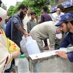 A large number of citizens including women and children crowd around a public water point to collect drinking water in containers and jerry cans