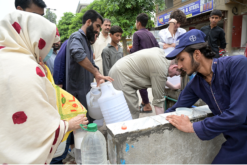 A large number of citizens including women and children crowd around a public water point to collect drinking water in containers and jerry cans