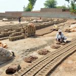 A worker shapes raw clay bricks by hand while rows of freshly moulded bricks are left to dry under the sun at a traditional brick kiln on the outskirts of the city