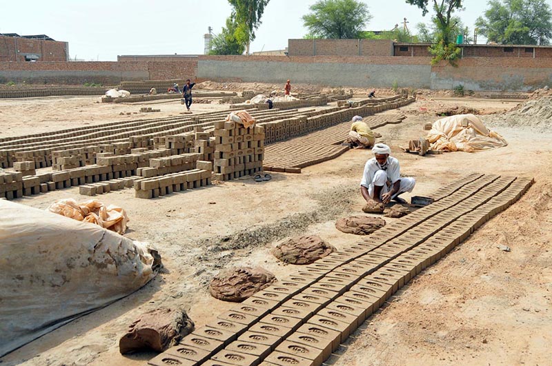 A worker shapes raw clay bricks by hand while rows of freshly moulded bricks are left to dry under the sun at a traditional brick kiln on the outskirts of the city