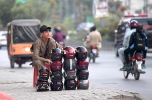 A young vendor is waiting for customers to sell safety helmets displayed on the footpath along Murree Road.