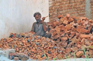 A labourer crushes old bricks into smaller pieces with a hammer for reuse as construction material at a building site to earn a livelihood. APP/QSM/TZD