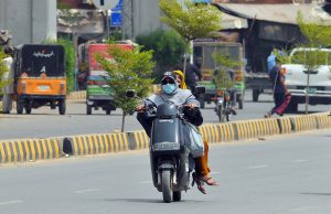 A woman rides an electric scooty with a companion along Water Works Road, wearing a face mask to protect herself from dust and the hot weather while heading to her destination in the city.
