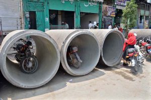 Motorcyclists park their bikes inside large concrete pipes placed along Lari Adda Road for an ongoing construction project.