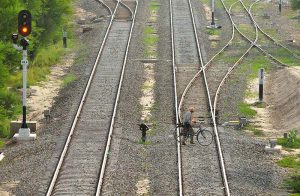 A person along with his bicycle is crossing railway tracks.