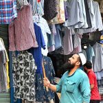 A vendor arranges colorful shirts outside his shop to attract customers at Anarkali Bazaar
