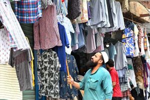 A vendor arranges colorful shirts outside his shop to attract customers at Anarkali Bazaar