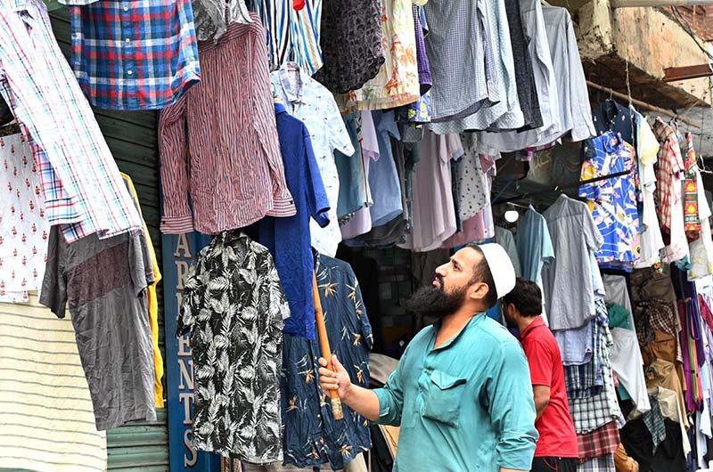A vendor arranges colorful shirts outside his shop to attract customers at Anarkali Bazaar