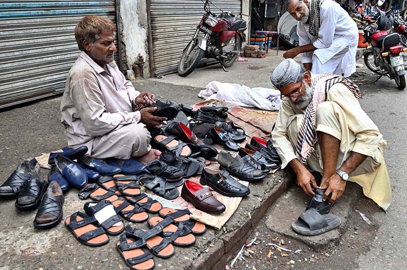 An elderly man buys shoes from a roadside vendor during routine business activity in the city
