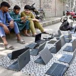Vendors sell used laptops along Hall Road during routine business activity in the city