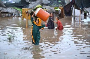 A girl carries a water container on her head while wading through floodwater after heavy monsoon rains inundated a makeshift settlement in the provincial capital.