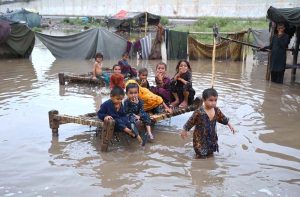 A girl carries a water container on her head while wading through floodwater after heavy monsoon rains inundated a makeshift settlement in the provincial capital.