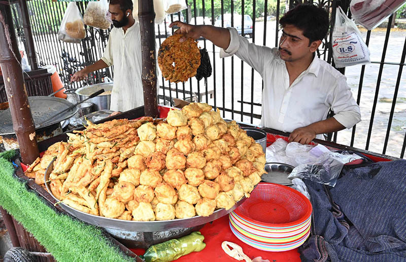 A street vendor prepares and sells freshly fried pakoras and besan naan on Lawrence Road as rainy weather boosts demand for traditional hot snacks