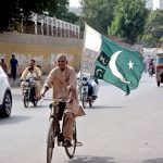 A man rides a bicycle carrying the national flag through the city, expressing his love and patriotism for Country