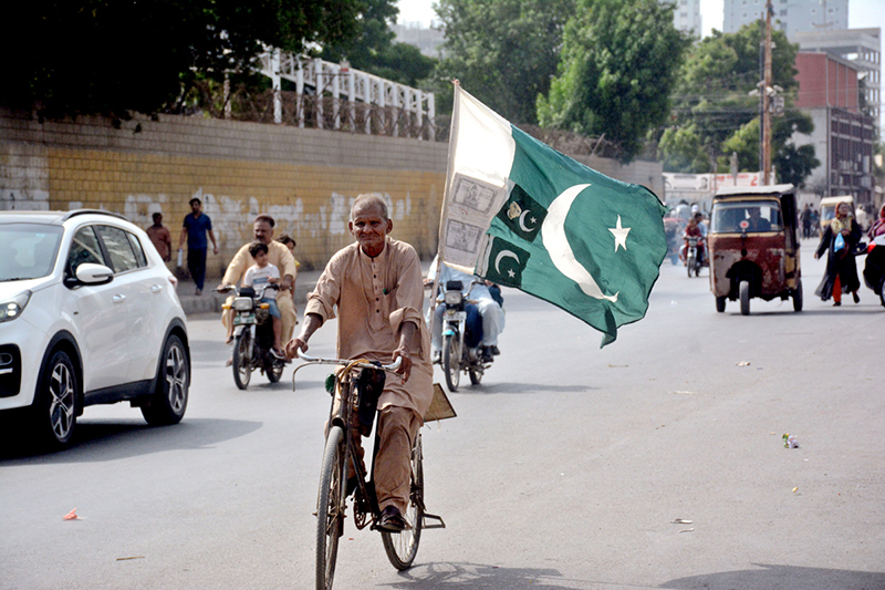 A man rides a bicycle carrying the national flag through the city, expressing his love and patriotism for Country