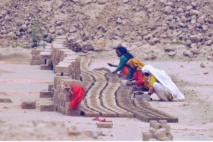 Women workers molding and arranging freshly made clay bricks for drying at a brick kiln on the outskirts of the city, earning their livelihood during a hot day in the city.