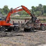 Labourers loading soil on tractor trolley with the help of machine near bypass road to supply to the customers