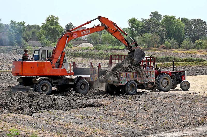 Labourers loading soil on tractor trolley with the help of machine near bypass road to supply to the customers