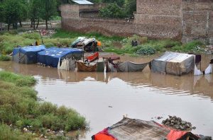 A man carries his household belongings to a safer area after heavy monsoon rains inundated a makeshift settlement, forcing families to relocate from flood-affected homes.