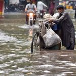 An elderly man pushes his bicycle laden with household items through a flooded road following heavy rainfall in the provincial capital