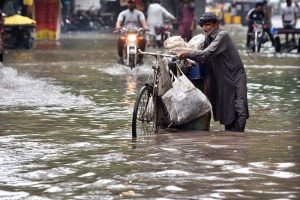 An elderly man pushes his bicycle laden with household items through a flooded road following heavy rainfall in the provincial capital
