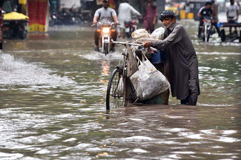An elderly man pushes his bicycle laden with household items through a flooded road following heavy rainfall in the provincial capital