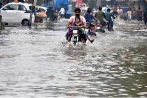 An elderly man pushes his bicycle laden with household items through a flooded road following heavy rainfall in the provincial capital