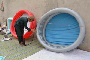 A vendor inflates and arranges colorful children's inflatable swimming pools and water play tubs for sale amid the summer heat at Double Road.