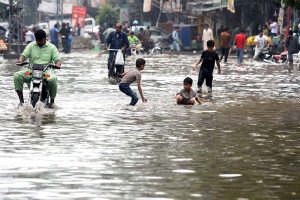 An elderly man pushes his bicycle laden with household items through a flooded road following heavy rainfall in the provincial capital