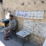 A vendor displays newspapers hanging on a wall for sale at a roadside stall