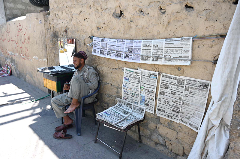 A vendor displays newspapers hanging on a wall for sale at a roadside stall