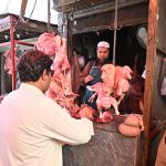 Customers purchase fresh mutton and chicken from a traditional butcher shop in a busy market